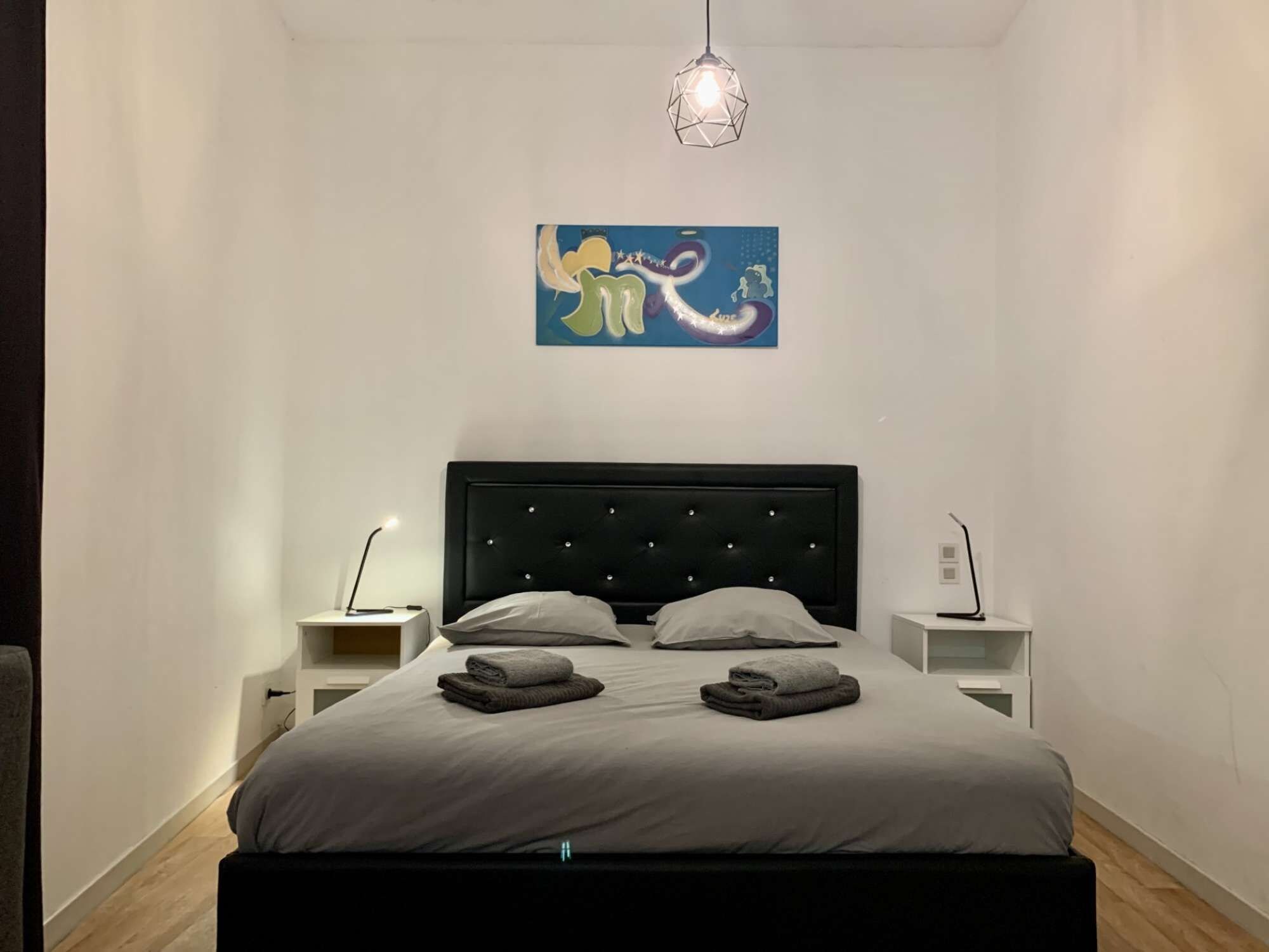 Ein Schlafzimmer mit einem Bett, zwei Nachttischen, einem an der Wand befestigten Kunstwerk und einer Pendelleuchte.