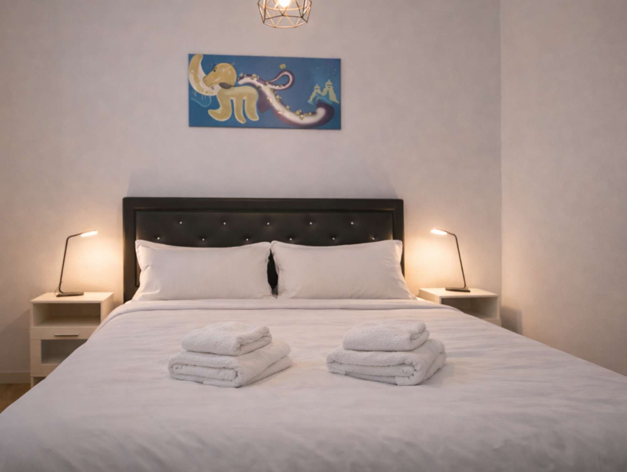 A neatly made bed with white linens and two folded towels on the bed.