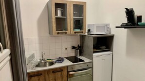 Ett kompakt kök med en diskho, spis, ugn och en mikrovågsugn som står på en hylla.