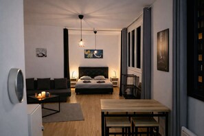A modern bedroom with a bed, bedside tables, a desk, and a dining area. - Studio Cosy - Hypercentre - Calme - 50m2 - Wifi (Graulhet)