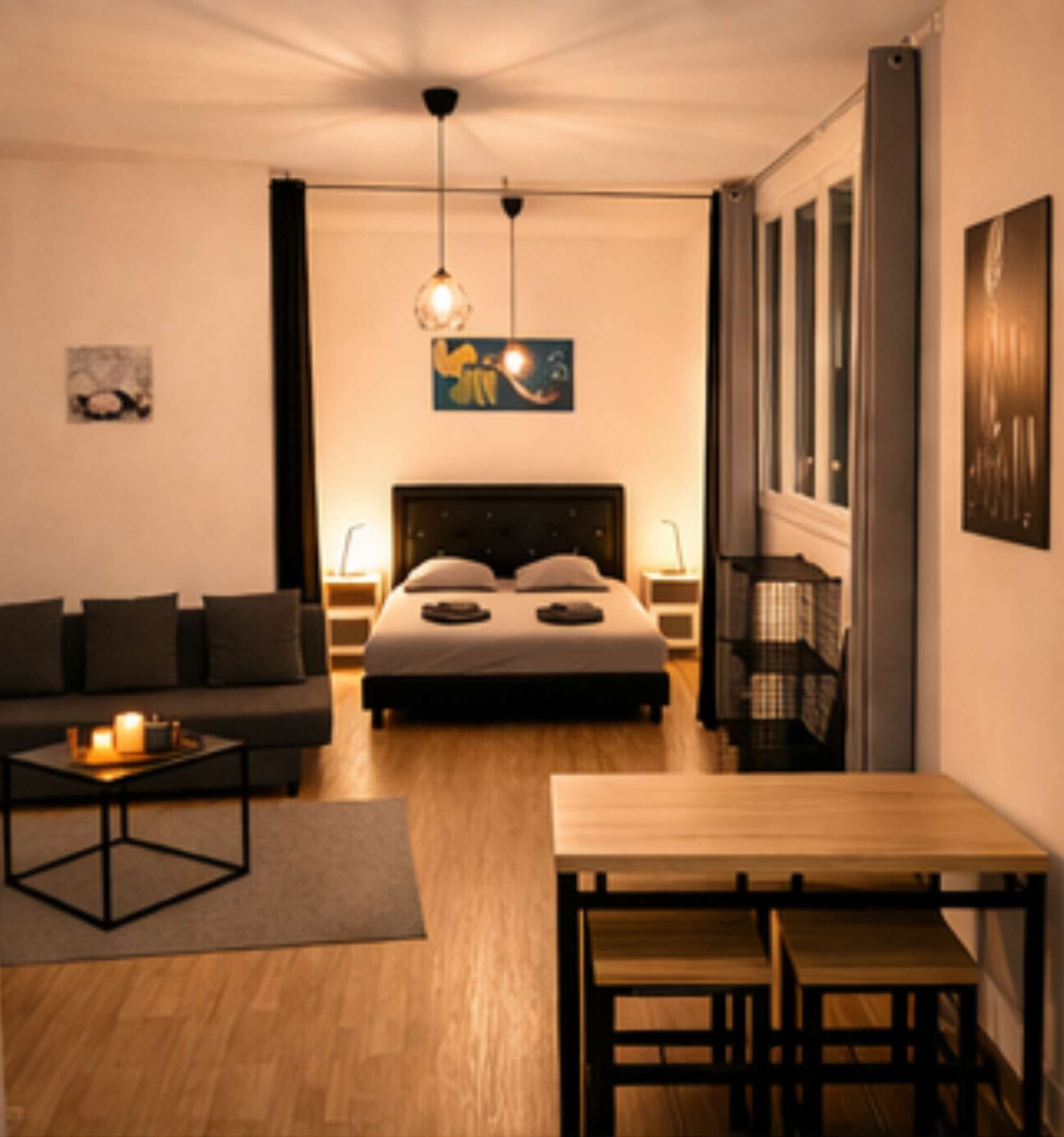 A modern bedroom with a bed, bedside tables, a sofa, a dining table, and a hanging light fixture.