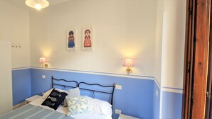 Een slaapkamer met een bed, nachtlampjes, een kledingkast en twee aan de muur hangende schilderijen.