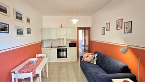 Een compacte leefruimte met een kitchenette, een eethoek met een tafel en stoelen, en een bank met een lamp.