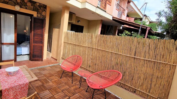 Een balkon met een stenen muur, een houten tafel en twee rode stoelen.