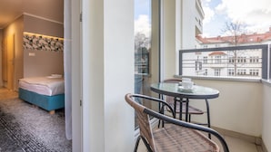 Quarto de hotel com cama, uma pequena mesa com cadeiras e vista para edifícios pela janela.