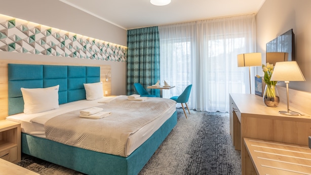 Quarto de hotel com uma cama grande, uma escrivaninha com abajur, uma cadeira e uma mesinha.