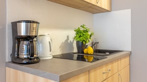 Uma cozinha com cafeteira, chaleira, pia e um vaso de planta.