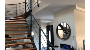 A modern staircase with wooden steps and black railings, leading to a room with a digital clock displaying 19:46.