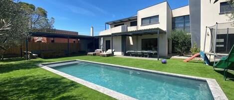 A modern house with a swimming pool, a covered patio, and a play area.