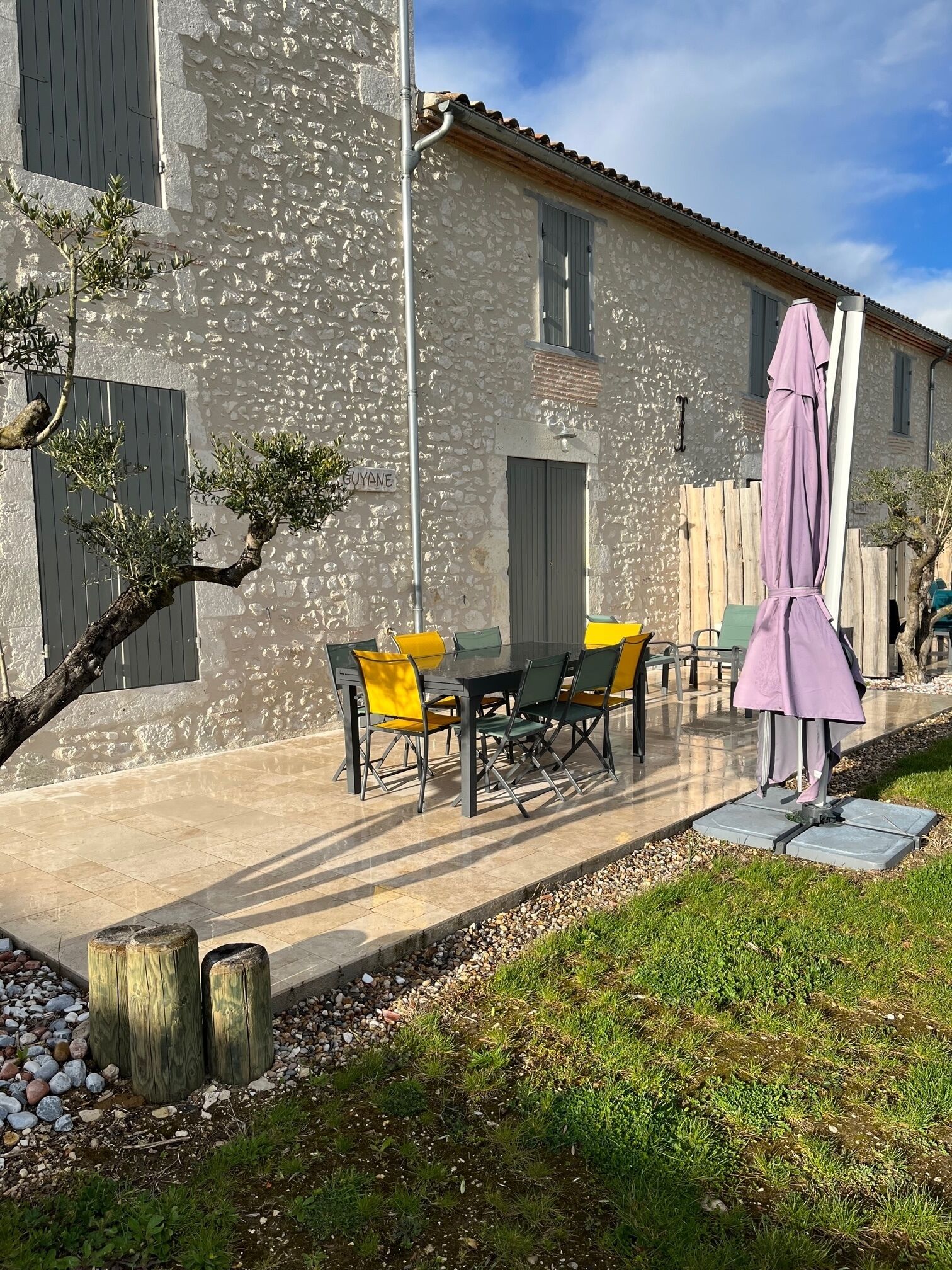 Ein Gebäude aus Stein mit einer Terrassenfläche, die einen Tisch und Stühle, einen Holzzaun und eine Rasenfläche umfasst.