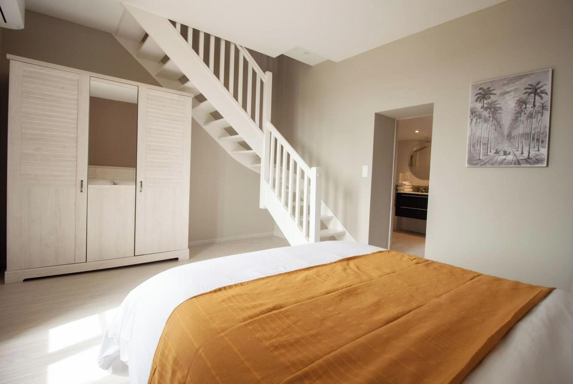 Un dormitorio con cama, una escalera, un armario y un baño visible a través de una puerta abierta.