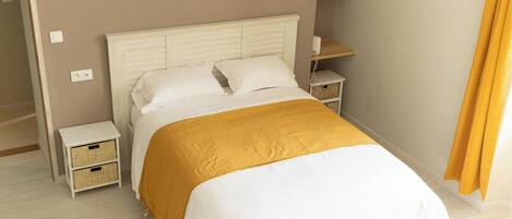 A bedroom with a white bed, a mustard-colored throw blanket, and two bedside tables with wicker baskets.