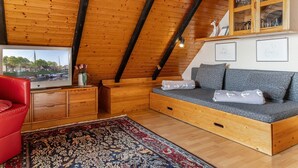A cozy loft bedroom with a wooden ceiling, a built-in sofa, a red chair, a TV, and a cabinet with glass doors. - The simply furnished apartment Am Seestern Carolinensiel awaits you (Carolinensiel)