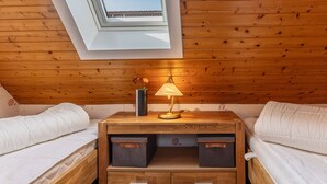 A cozy room with a sloped ceiling, wooden walls, a skylight, a bedside table with a lamp, and two beds. - The simply furnished apartment Am Seestern Carolinensiel awaits you (Carolinensiel)