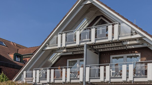 A modern building with a sloped roof, multiple windows, and a balcony with railings. - The simply furnished apartment Am Seestern Carolinensiel awaits you (Carolinensiel)