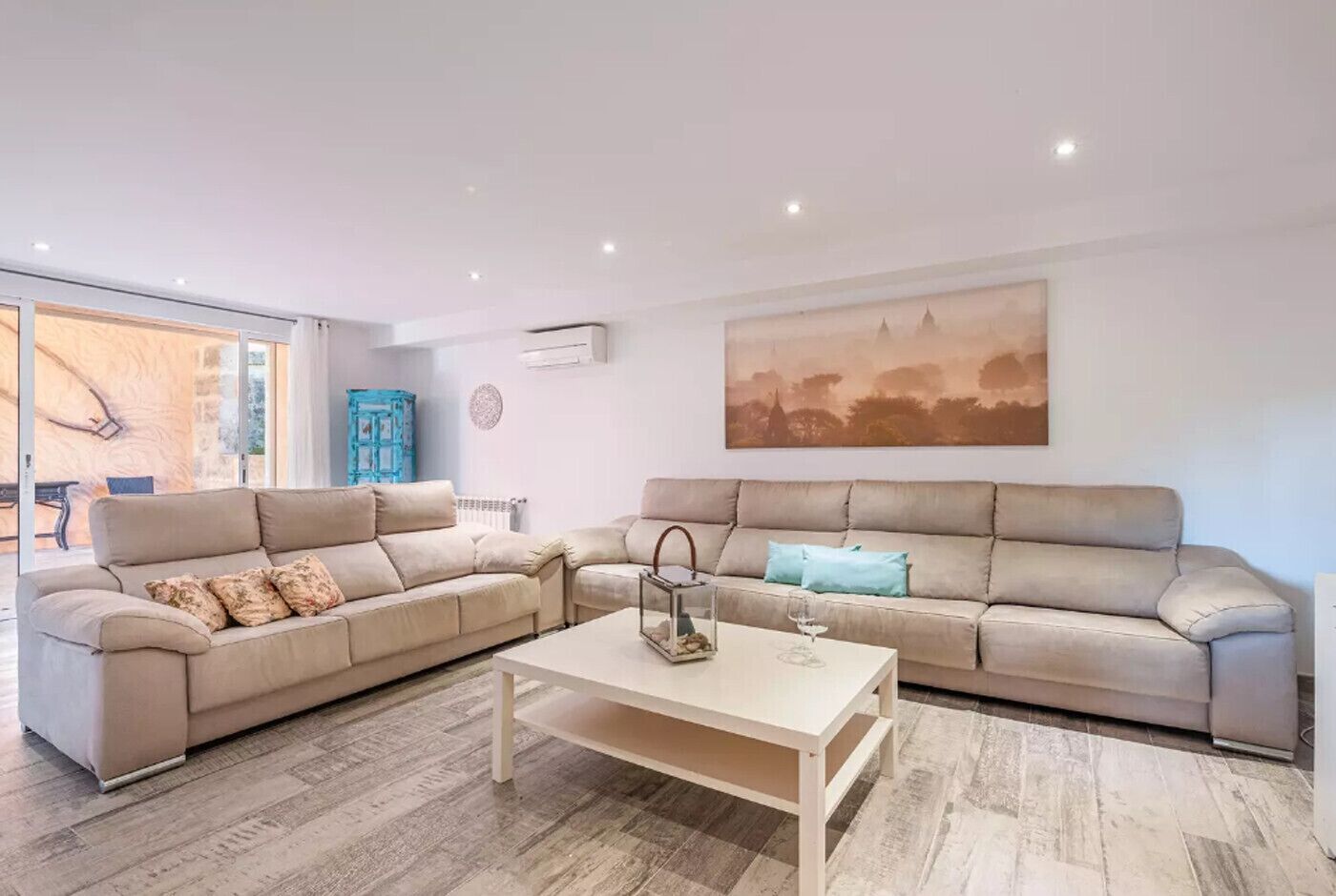 Una sala moderna con dos sofás beige, una mesa de centro blanca y un cuadro grande con un paisaje en la pared.