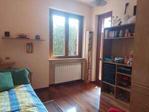 Una habitación con una cama, ventana, radiador, estantería y puerta.