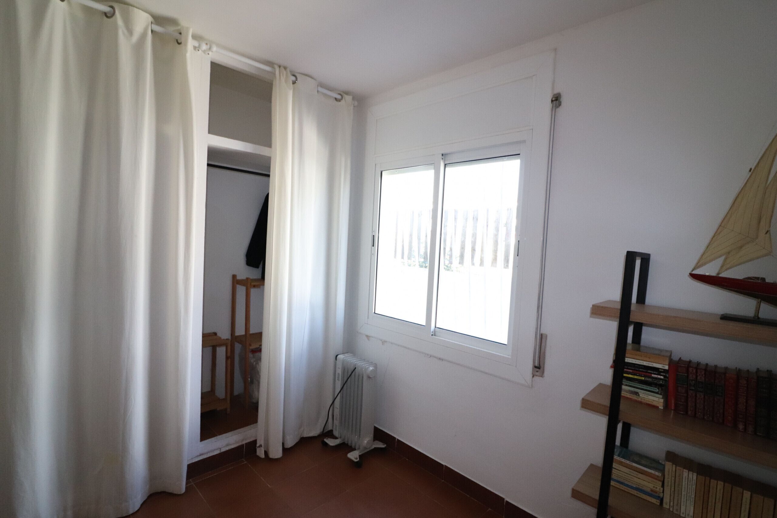 A room with a window, a radiator, a wooden chair, and a bookshelf.
