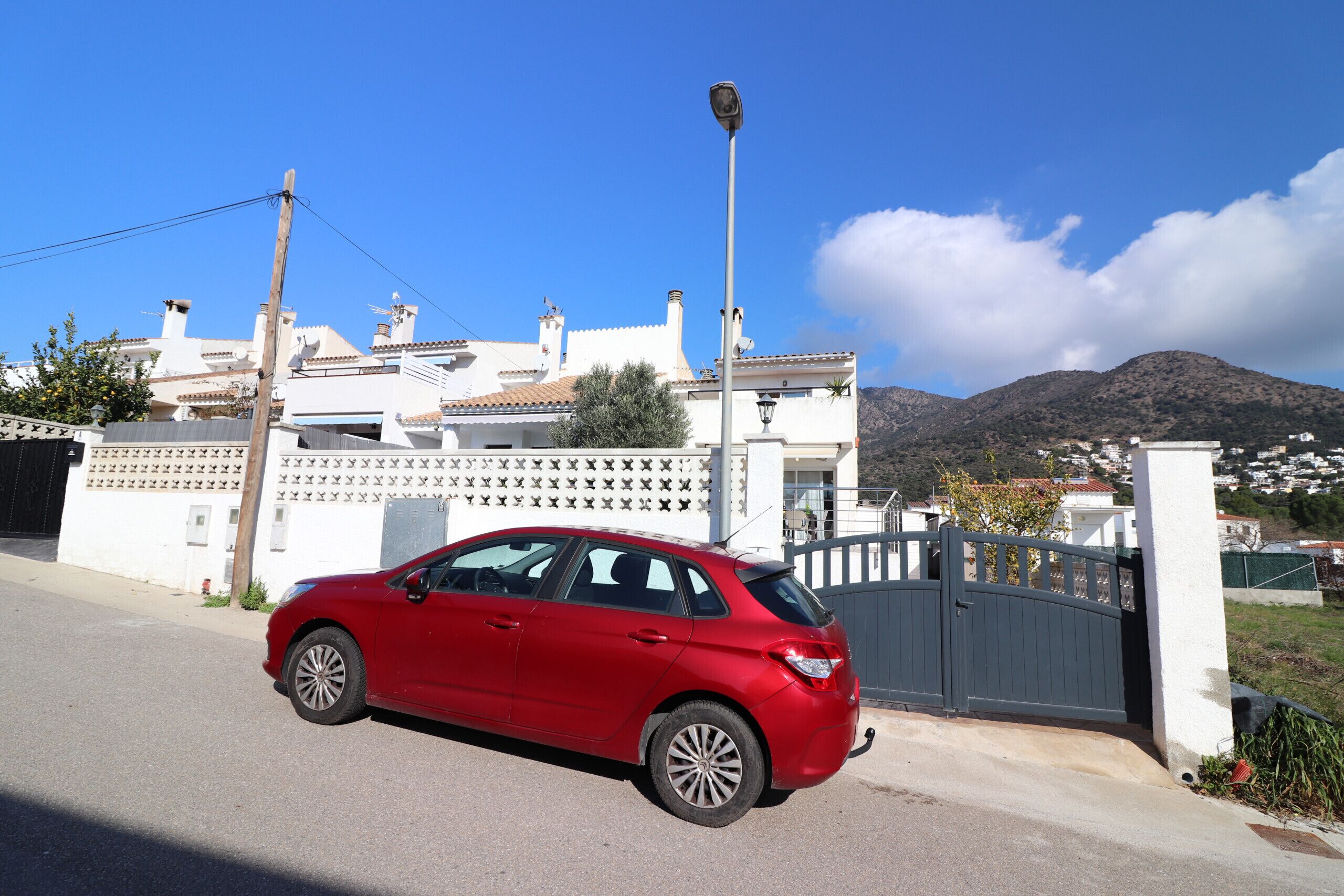 A red car parked in front of a white building with a gated entrance and a street lamp.