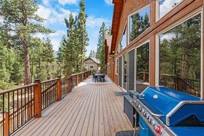 A wooden deck with a barbecue grill, a table with chairs, and a view of a forested area.