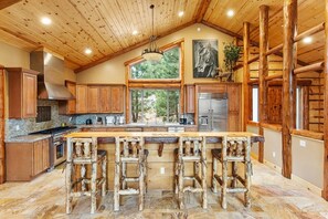 A spacious kitchen with a large island, wooden bar stools, and a stone floor.