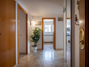 A hallway with wooden doors, a potted plant, a tiled floor, and a view into a kitchen area.
