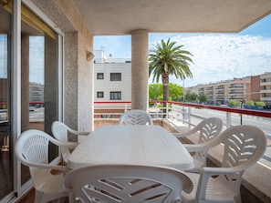A balcony with a table and chairs, a palm tree, and buildings in the background.