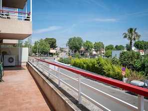 A balcony with a red railing overlooking a street with cars and buildings.