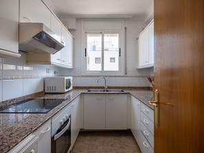 Une cuisine compacte avec des meubles blancs, un plan de travail en granit, un four à micro-ondes encastré et une fenêtre donnant sur des immeubles.