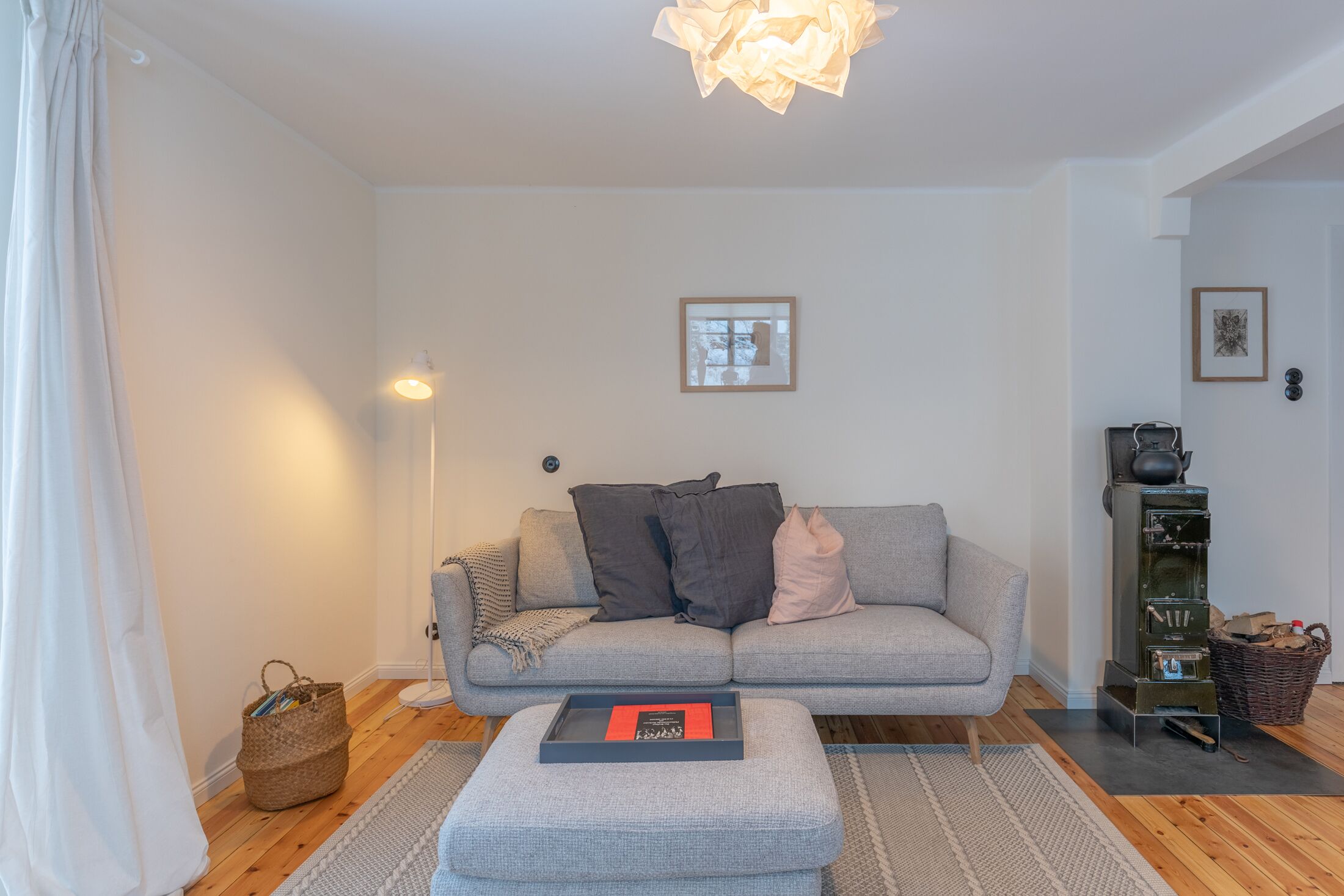 Ein modernes Wohnzimmer mit einem grauen Sofa, einem kleinen Hocker, einer Stehlampe und einem Kamin.