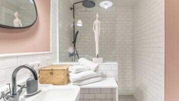 Ein Badezimmer mit weißem Waschbecken, einem Spiegel, einer Dusche mit Duschbrausehandstück und einem Handtuchhalter.