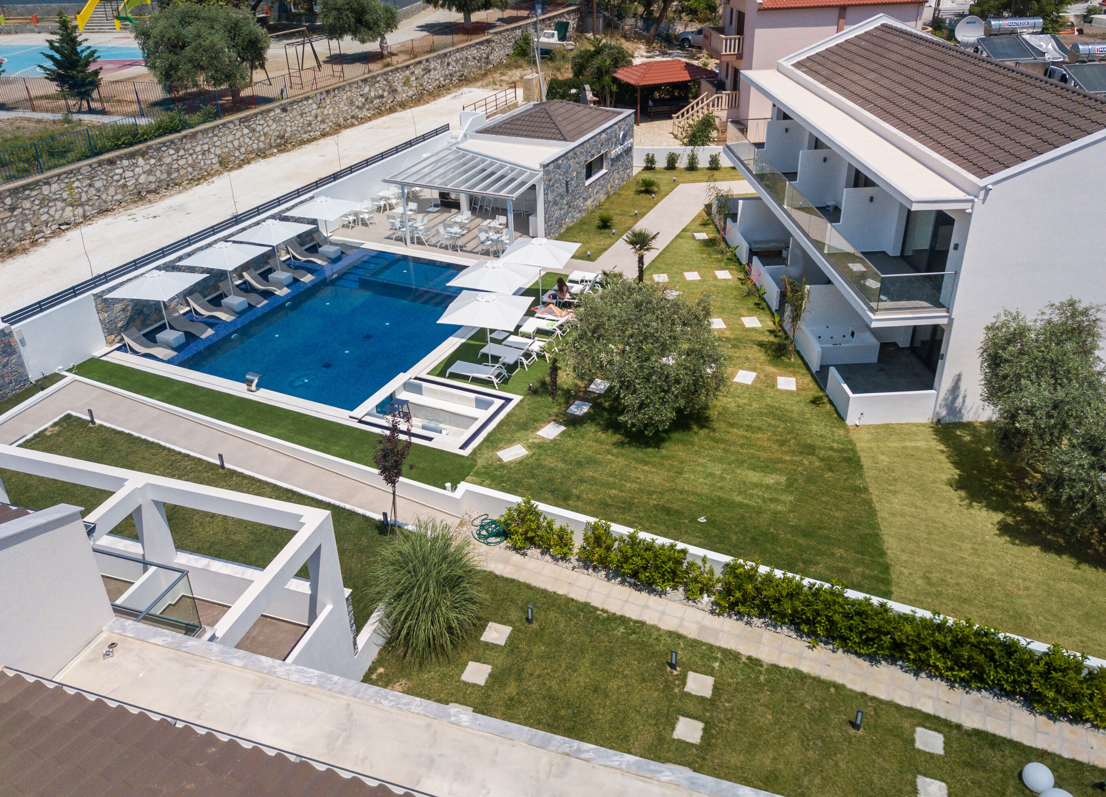 A modern hotel with a large swimming pool, outdoor seating, and a well-maintained lawn.
