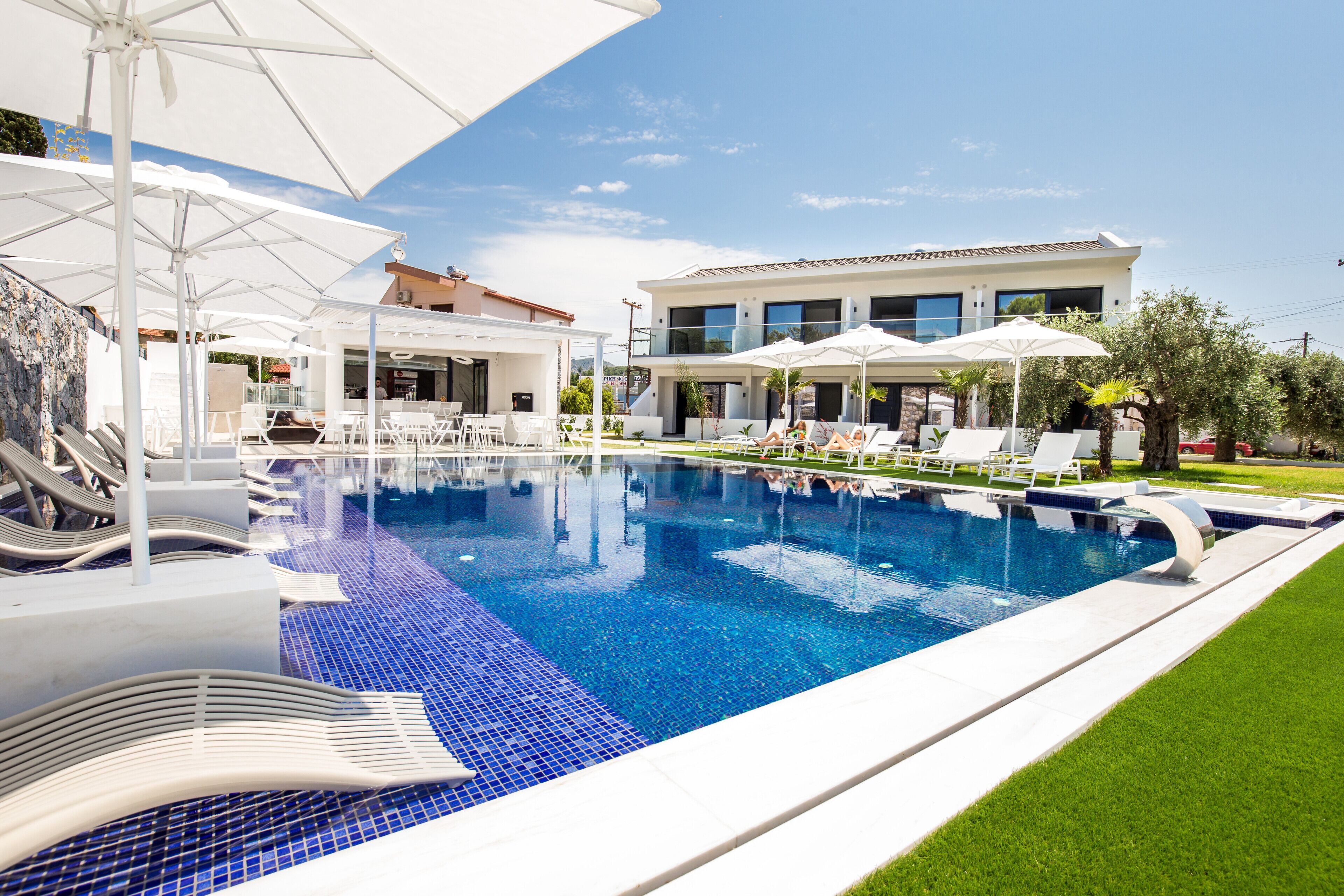 A swimming pool with lounge chairs and umbrellas, a modern building with large windows, and a well-maintained lawn.
