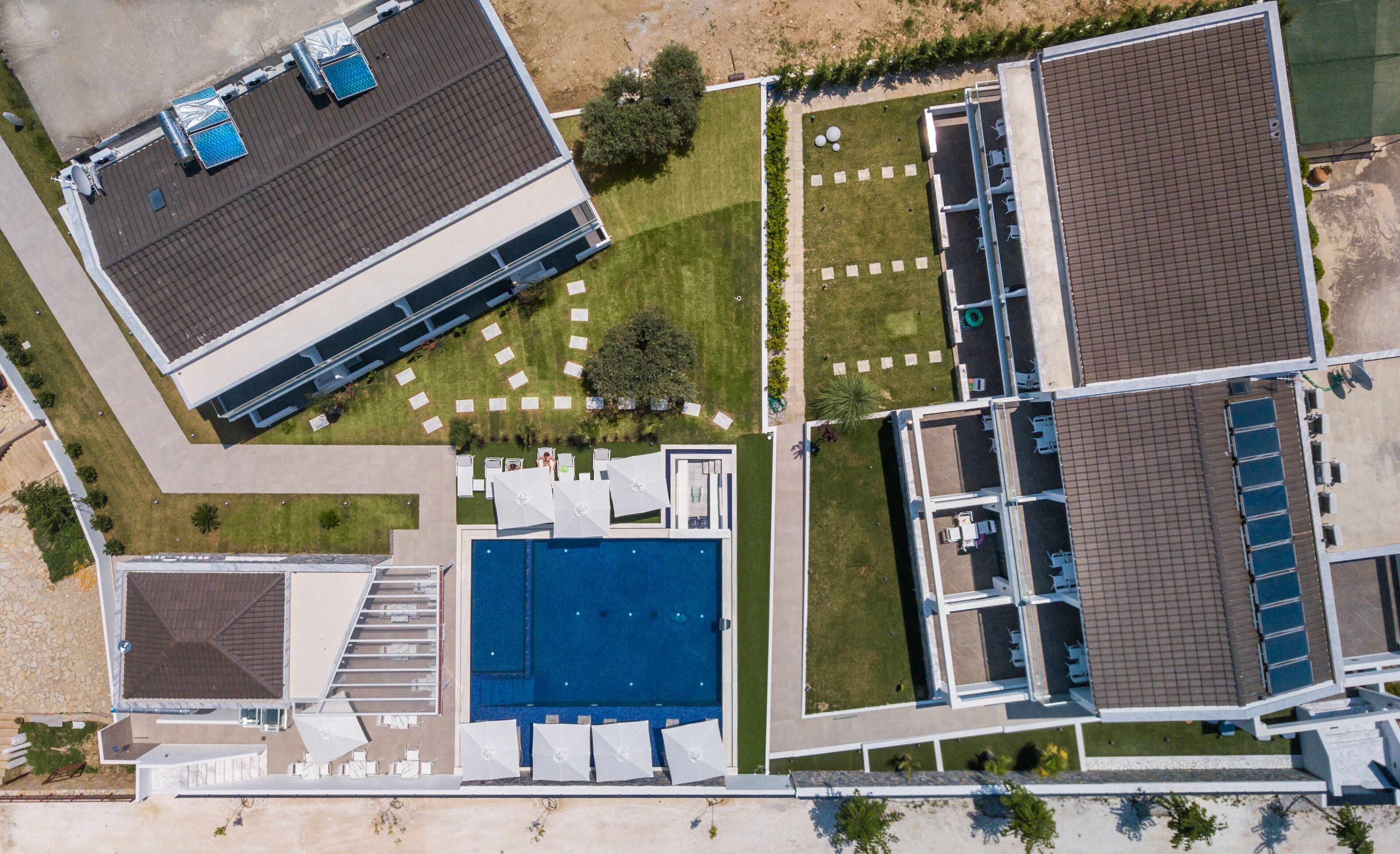 An aerial view of a hotel with a swimming pool, multiple outdoor seating areas, and a parking lot.
