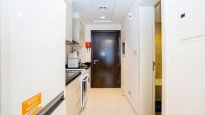 A narrow hallway with a kitchen area on the left, a wooden door at the end, and a bathroom visible through an open door on the right.