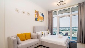 A modern bedroom with a sofa, a bed, and a large window offering a city view.