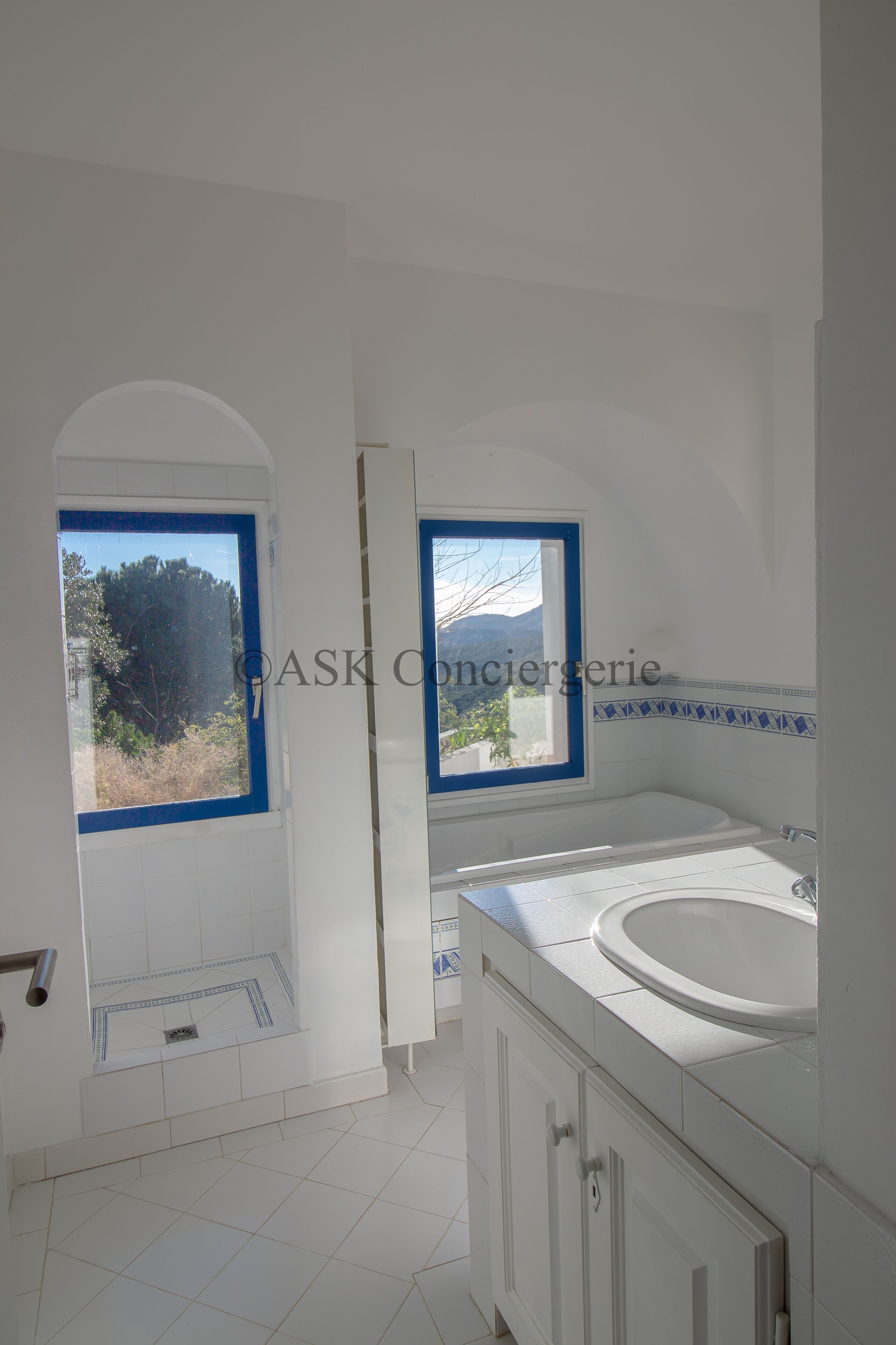 A bathroom with a bathtub, a window with a view of trees, and a tiled floor.