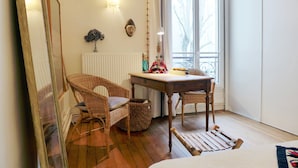 Een kamer met een houten vloer, een tafel met stoelen, een radiator, een raam met uitzicht en een spiegel.