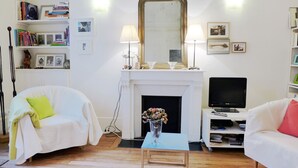 Een woonkamer met een open haard, twee witte banken, een salontafel en een tv-meubel.