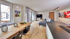 Un salon moderne avec une table à manger en bois, un canapé gris et un grand téléviseur.