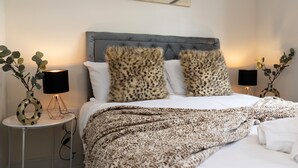 A neatly made bed with a leopard print throw blanket, two matching leopard print pillows, and a grey upholstered headboard. There are two bedside tables with lamps, one of which has a decorative vase with green leaves. - 8 Avery Gardens (Darlington)