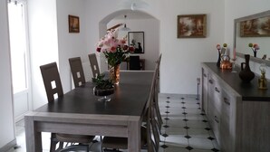 A dining area with a wooden table, chairs, a vase with flowers, and a tiled floor. - NANOU residence (Mont-Dore)