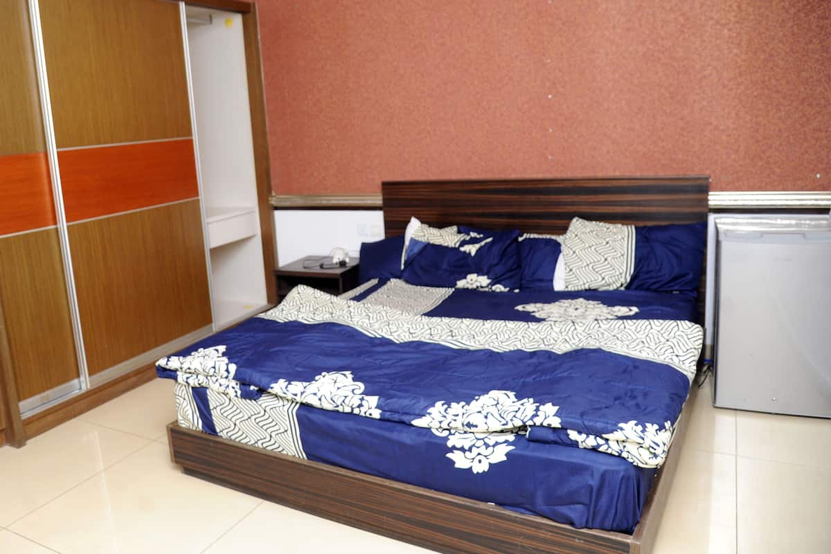 Un dormitorio con cama, armario, mesita de noche y un refrigerador pequeño.