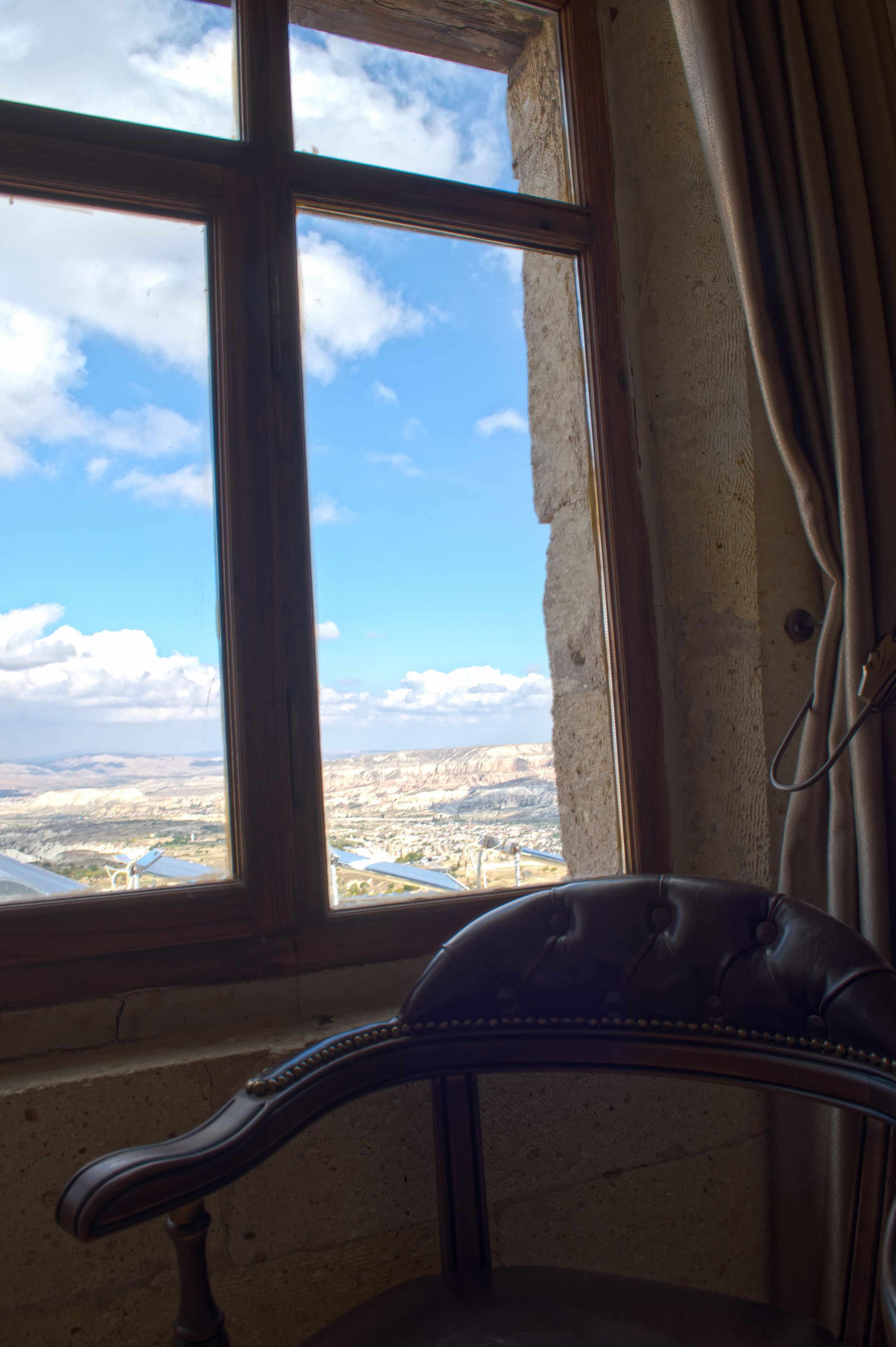 A room with a large window overlooking a landscape, a leather armchair, and a curtain.