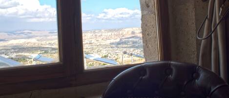 A room with a large window overlooking a landscape, a leather armchair, and a curtain.