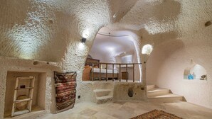 A room with a stone wall, a wooden staircase, and a patterned rug. - Ages in Cappadocia (Nevsehir)