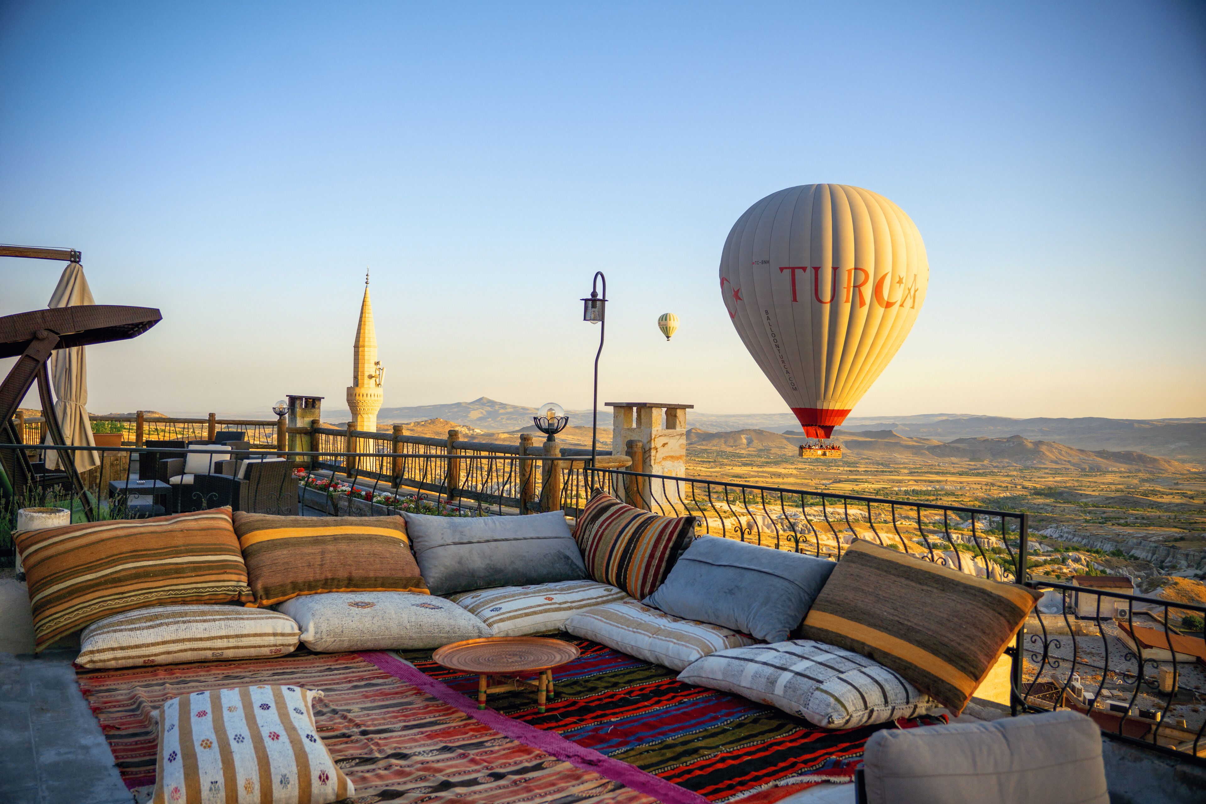 A rooftop terrace with a sofa set, a view of the city, and a hot air balloon in the distance.