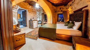 A rustic bedroom with a stone archway, a bed with a green cover, wooden furniture, and a view through the archway. - Ages in Cappadocia (Nevsehir)