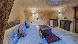 A cozy interior with a stone ceiling, a sofa with colorful cushions, a wooden table, and a patterned rug. - Ages in Cappadocia (Nevsehir)