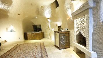 Una habitación con techo alto y texturizado, alfombra estampada, mueble de madera y chimenea decorativa.